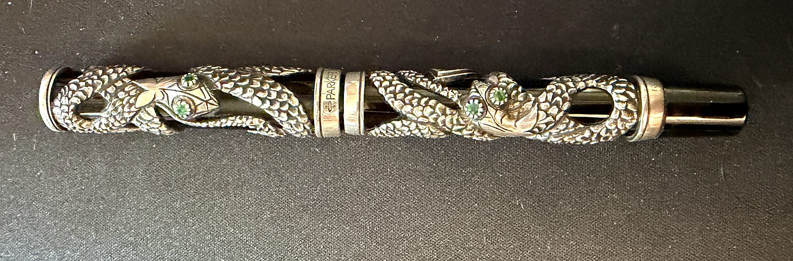 The Parker Snake fountain pen, capped: a sterling silver snake coiled around a black barrel and cap, with two heads meeting at the centre band and emeralds set as eyes.